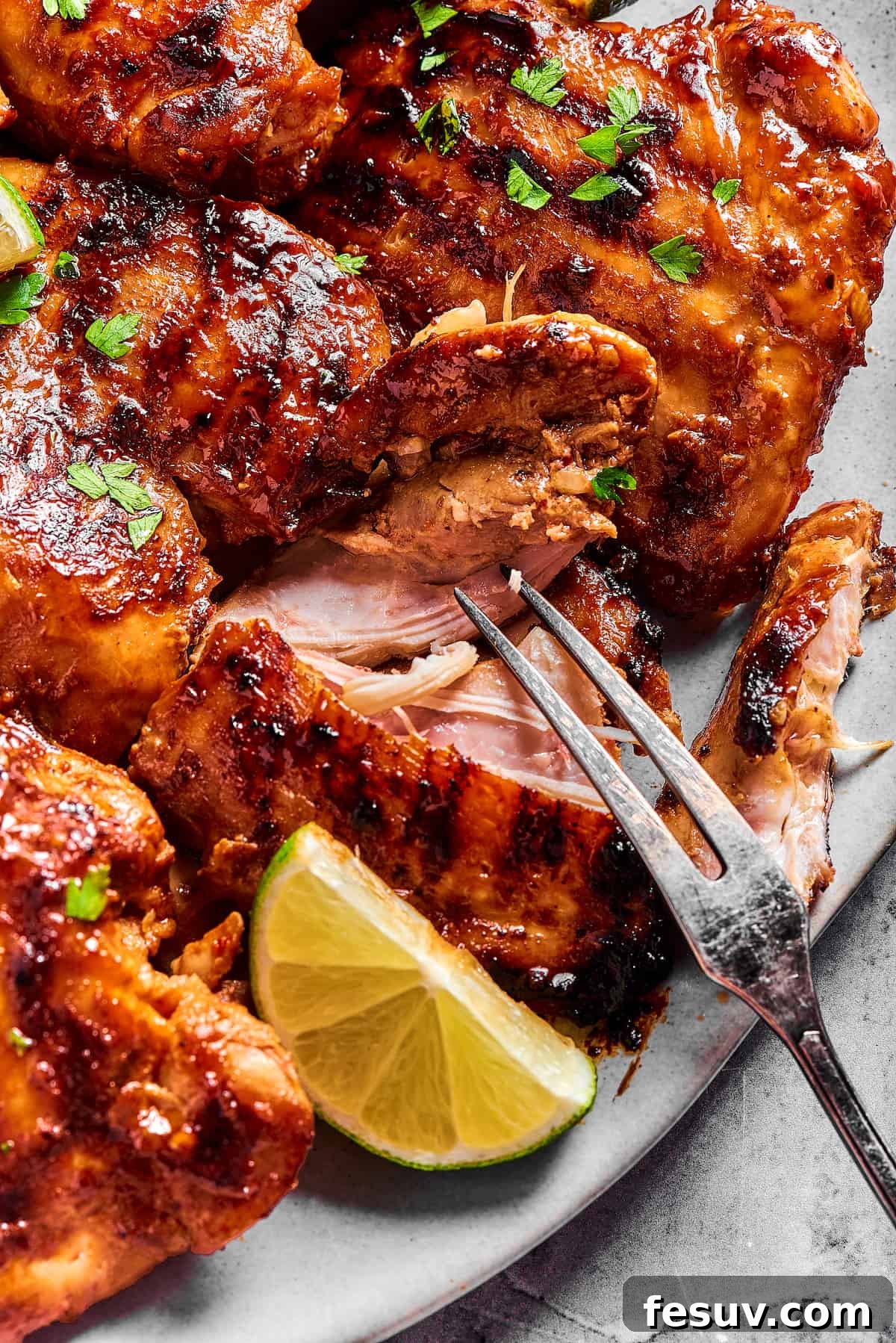 A close-up shot of a platter of grilled chicken, with one piece being gently pulled apart by a grilling fork, revealing its perfectly cooked, juicy interior texture.