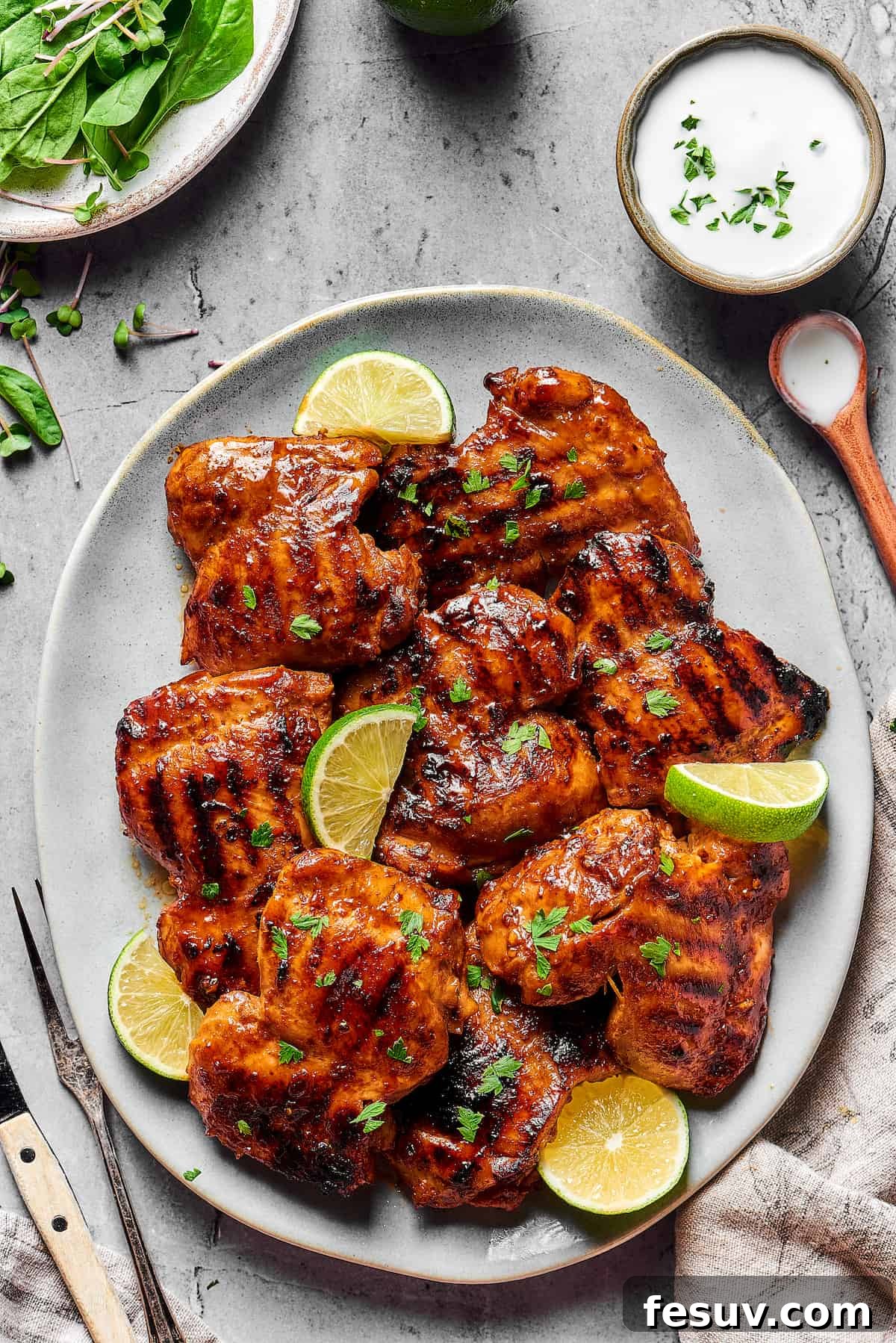 An oval platter generously filled with perfectly grilled chicken thighs, beautifully garnished with fresh parsley and vibrant lime wedges, ready for serving.