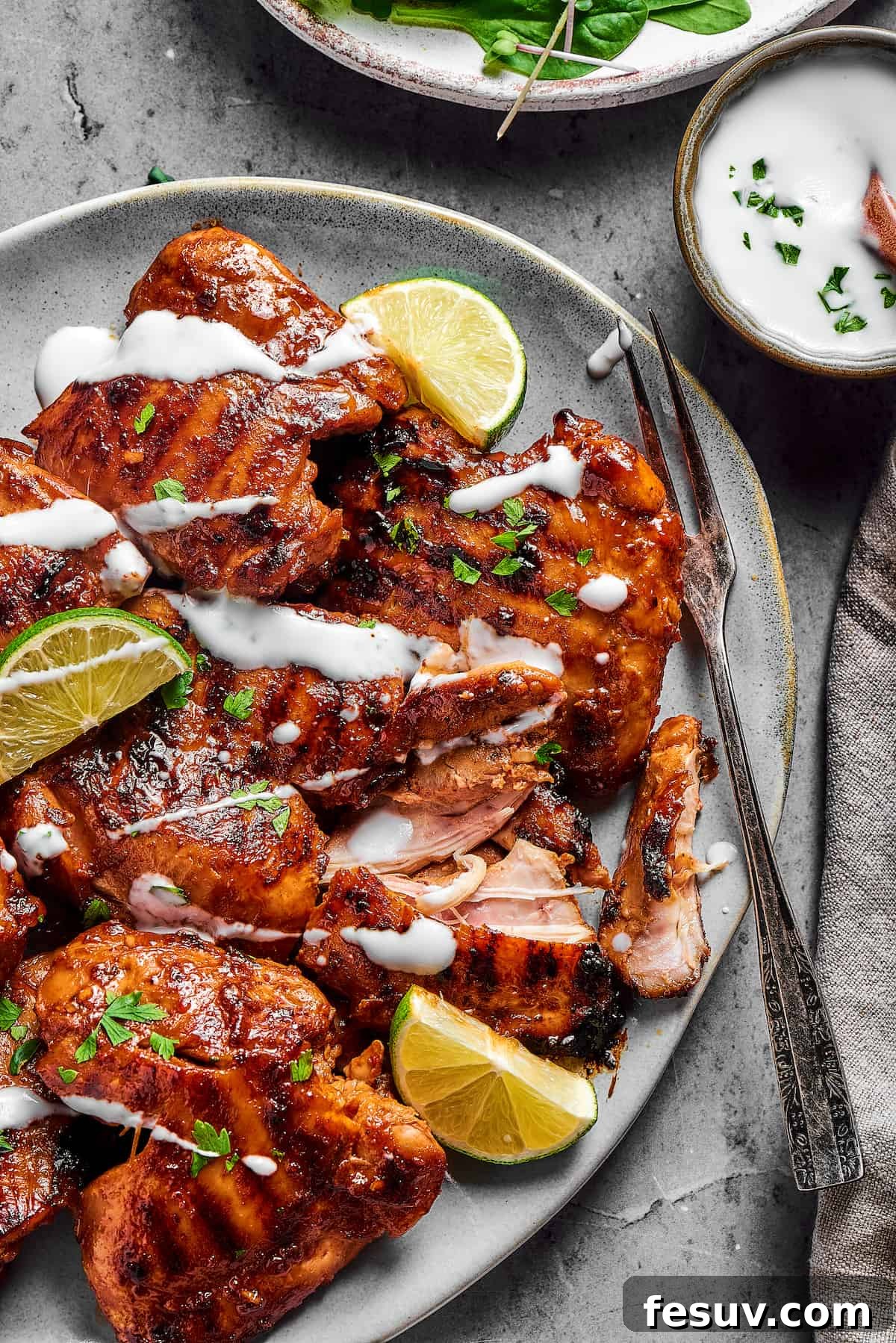 A serving dish abundantly filled with grilled chicken thighs, each piece beautifully garnished with a delicate drizzle of creamy yogurt and fresh herbs.