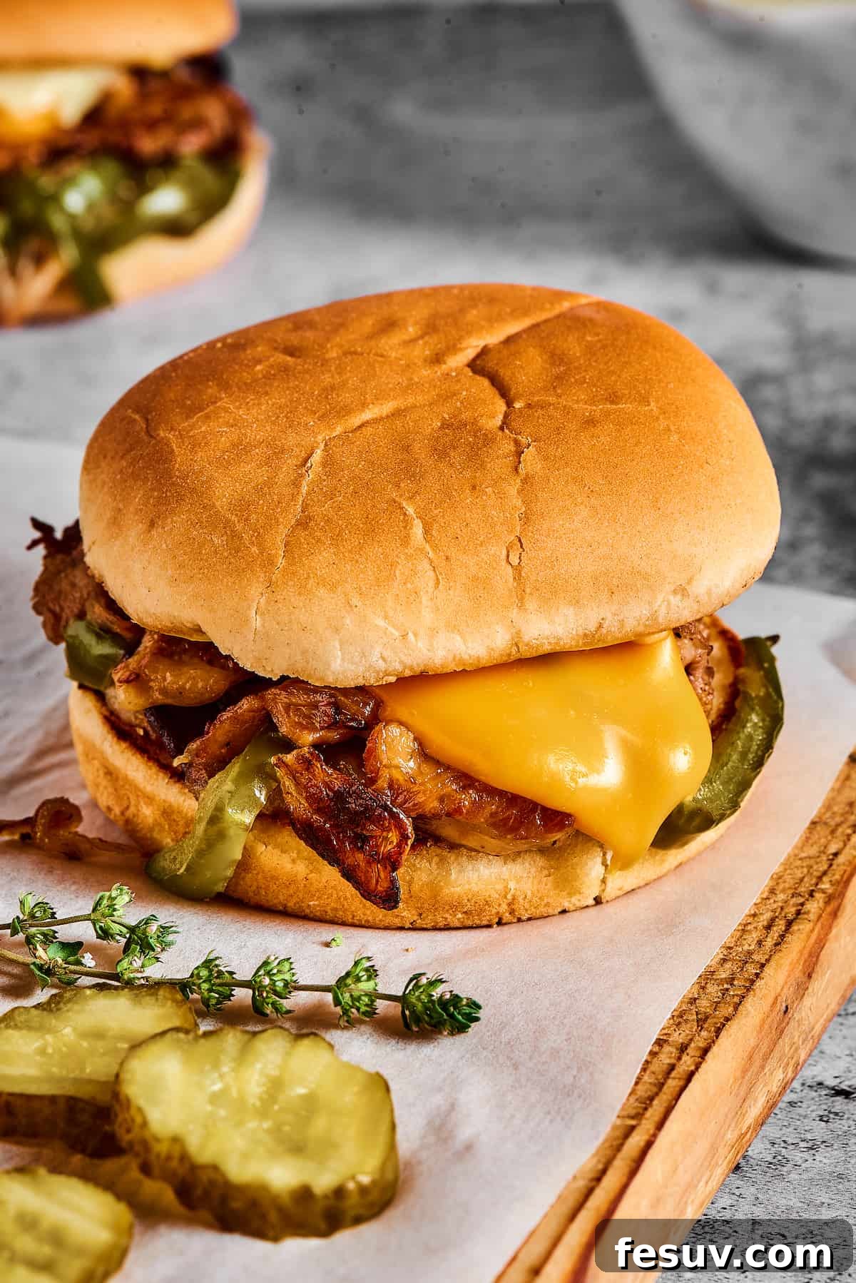 A steak sandwich on a hamburger bun with dill pickle chips and fresh thyme.