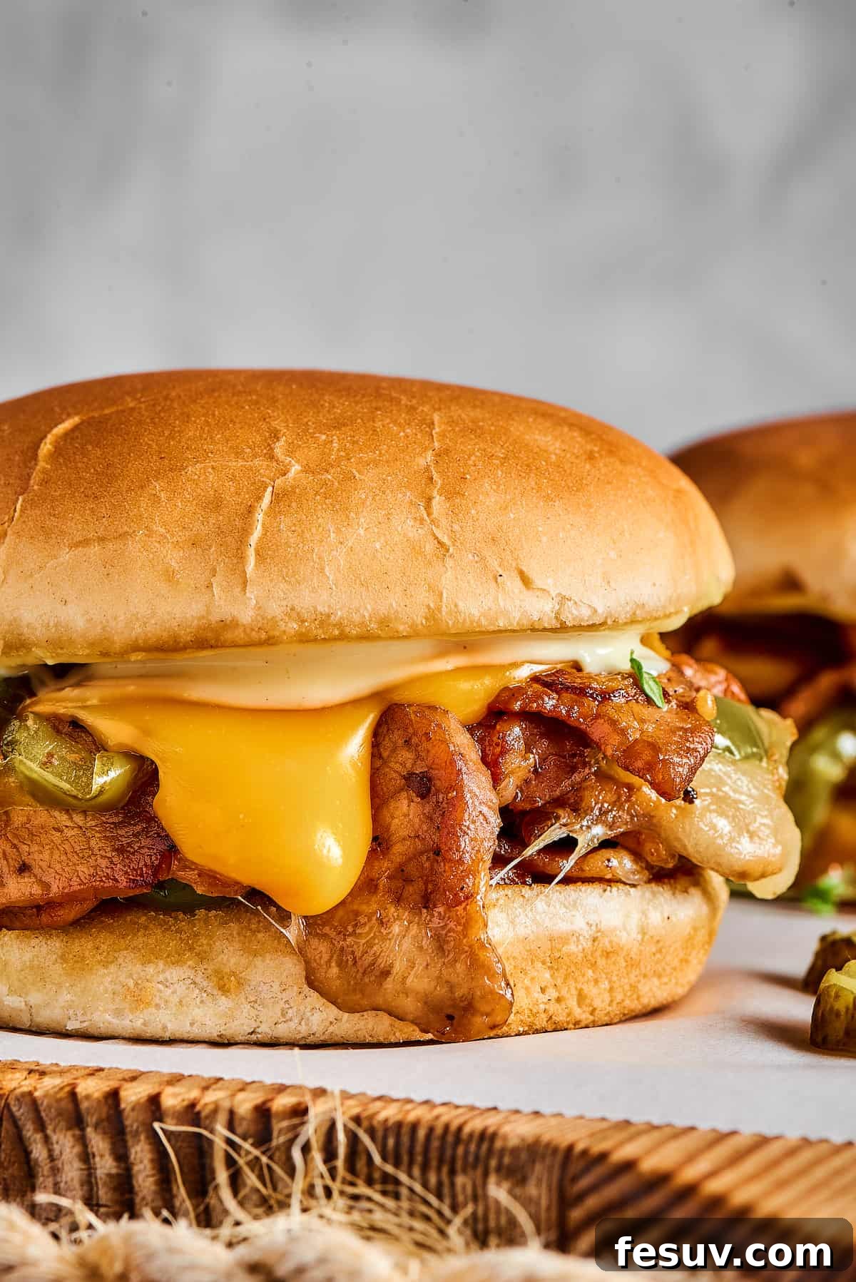 Philly cheesesteak burgers on a parchment-lined cutting board.