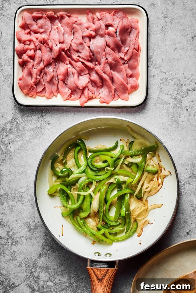 Overhead shot of a skillet of sauteing veggies, next to an enamel dish of sliced steak.
