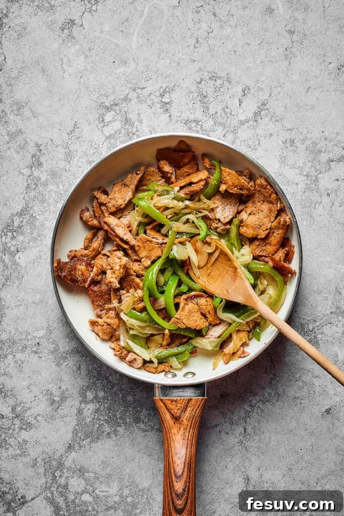 Sliced steak, onion, and bell pepper cooking in a skillet.