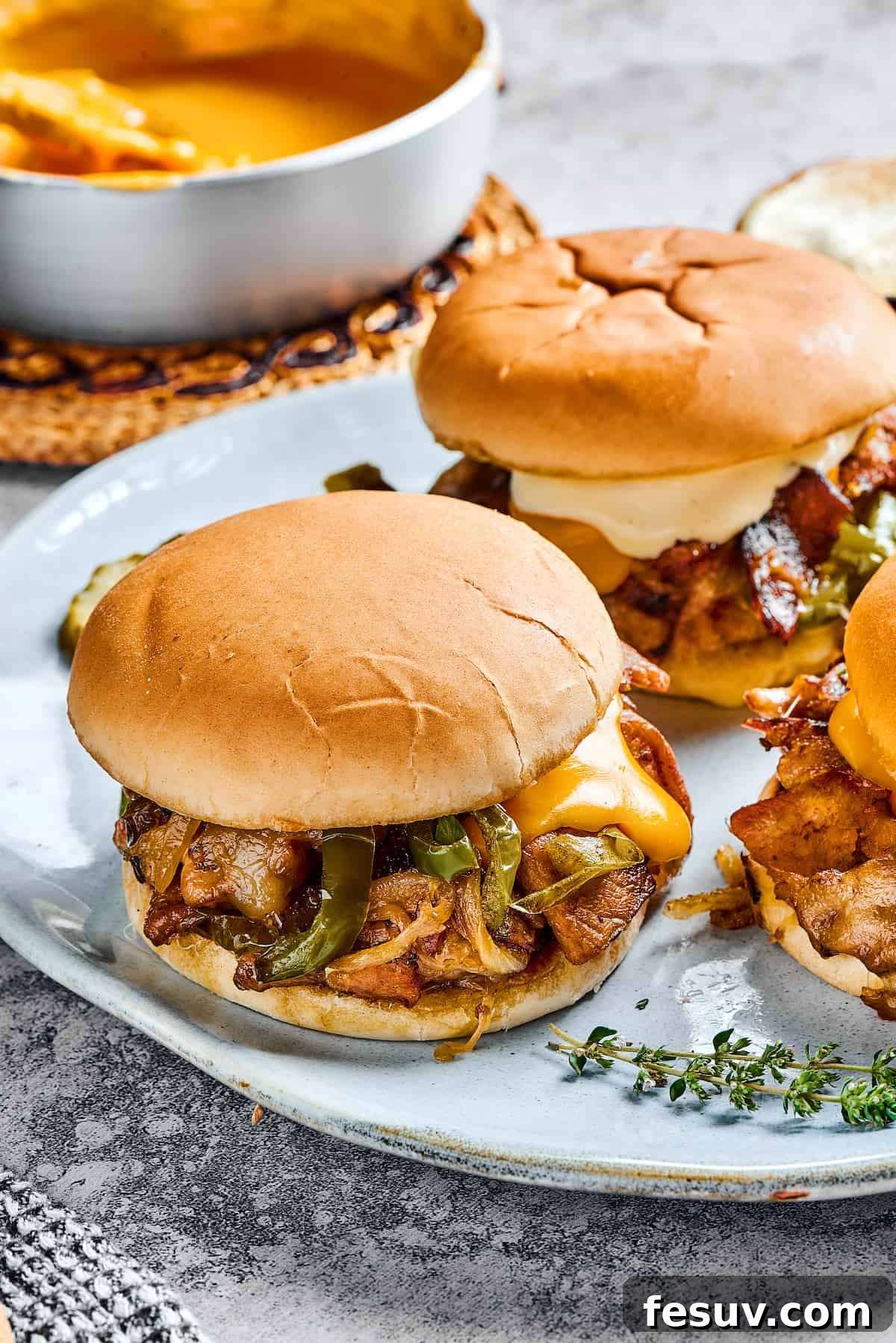 Two steak sandwiches with onions, melted cheese, and bell peppers.
