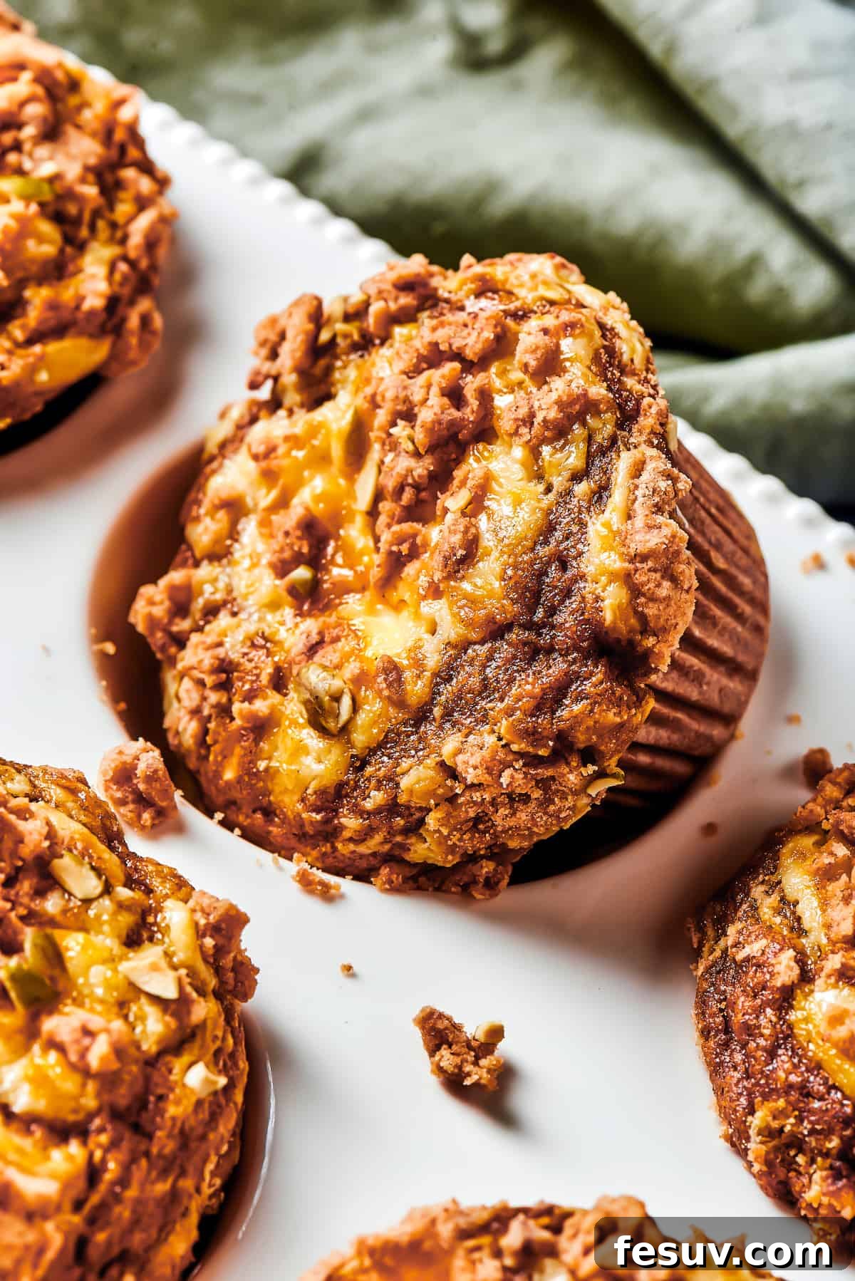 Pumpkin Cream Cheese Muffins are a heavenly mix of spiced pumpkin cake and smooth cream cheese swirl, with a buttery, streusel-like topping. A muffin tin with one muffin turned diagonally in its well. Small pieces of topping have fallen off onto the muffin tin.