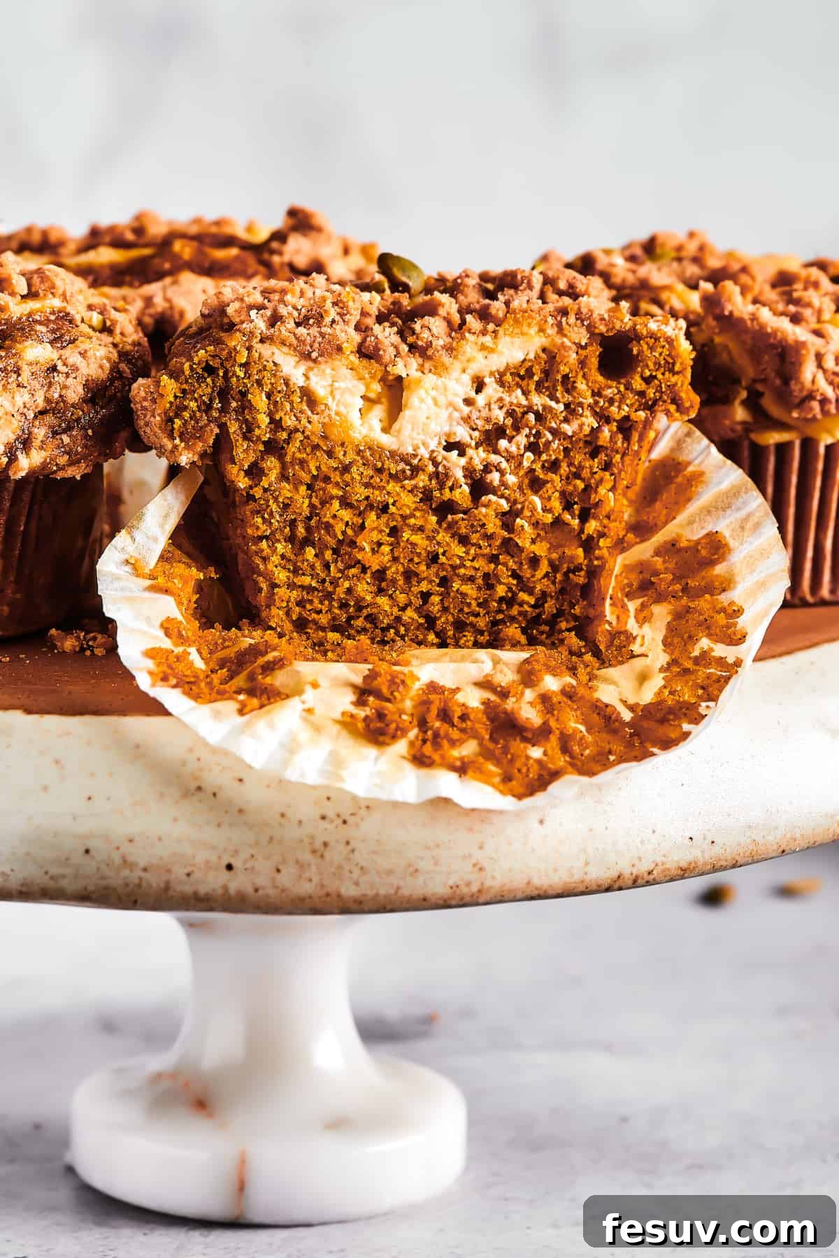 Pumpkin Cream Cheese Muffins are a heavenly mix of spiced pumpkin cake and smooth cream cheese swirl, with a buttery, streusel-like topping. Pumpkin muffins arranged on a cake stand.