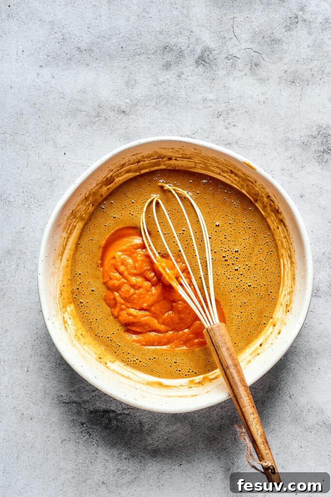 Cream Cheese Swirl Pumpkin Muffins 2 Wet muffin batter ingredients in a mixing bowl with a whisk, including pumpkin puree.