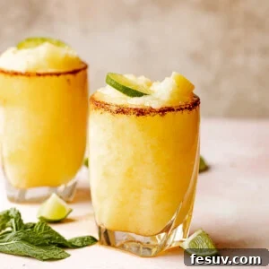 Two glasses of frozen pineapple margaritas with a chili salt rim garnished with lime and mint.
