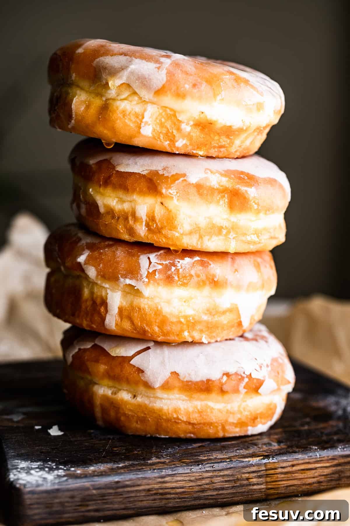 Four baked apple cider doughnuts stacked elegantly, with a warm, inviting brown backdrop.