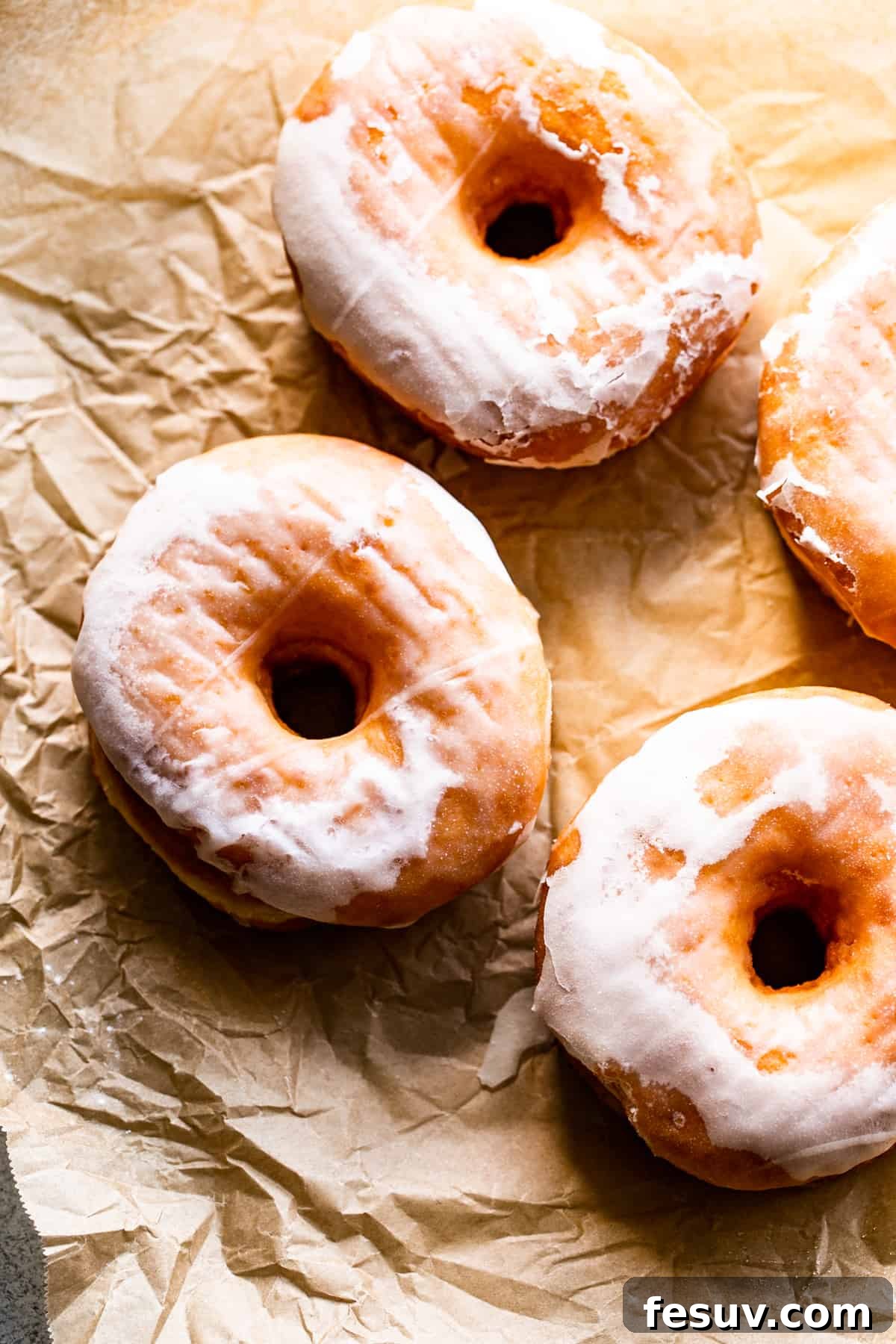 Three perfectly glazed apple cider doughnuts arranged on a light brown baking paper, showcasing their inviting texture.