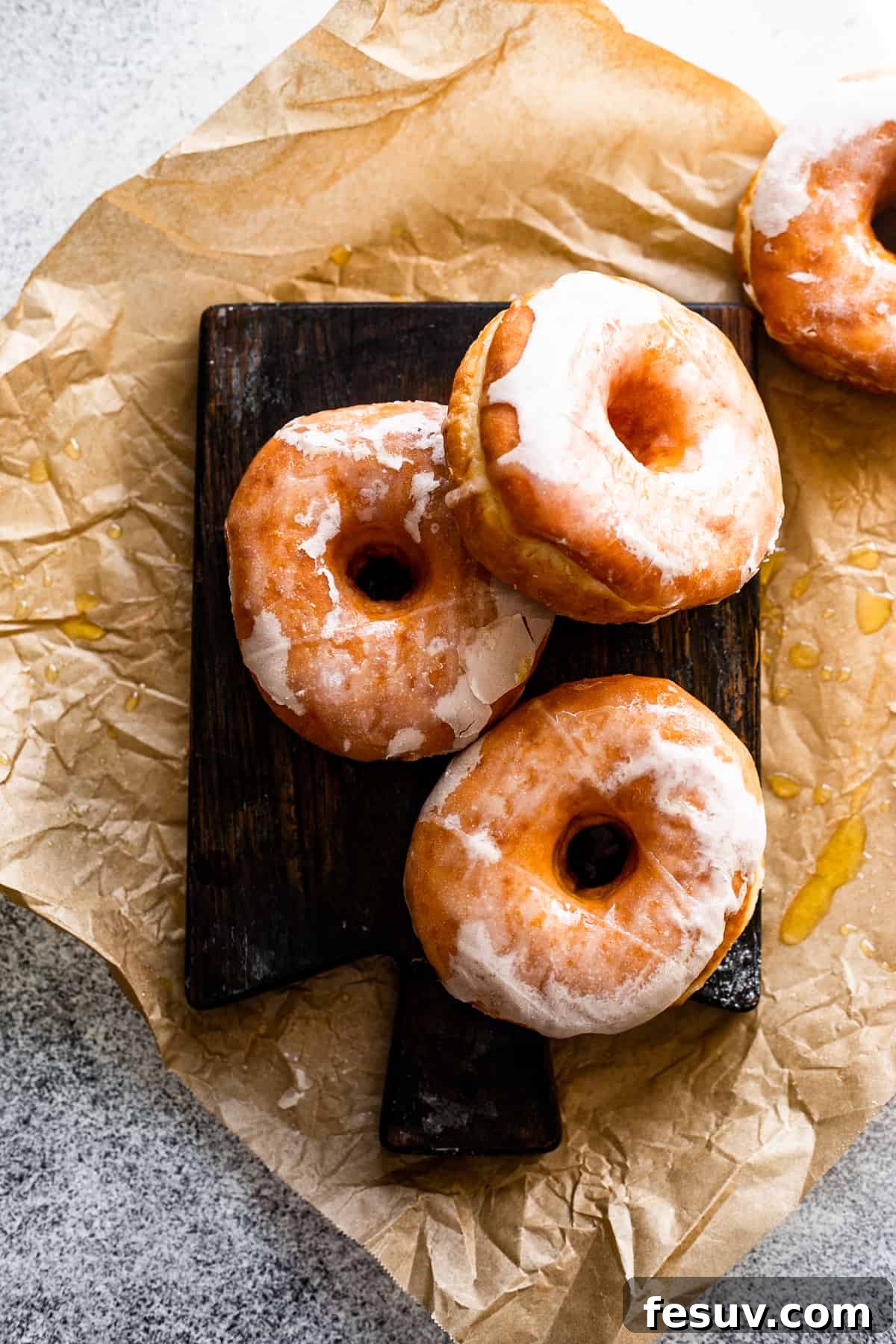 An overhead shot of three apple cider doughnuts neatly arranged on a dark wooden board, with one doughnut placed subtly to the side.