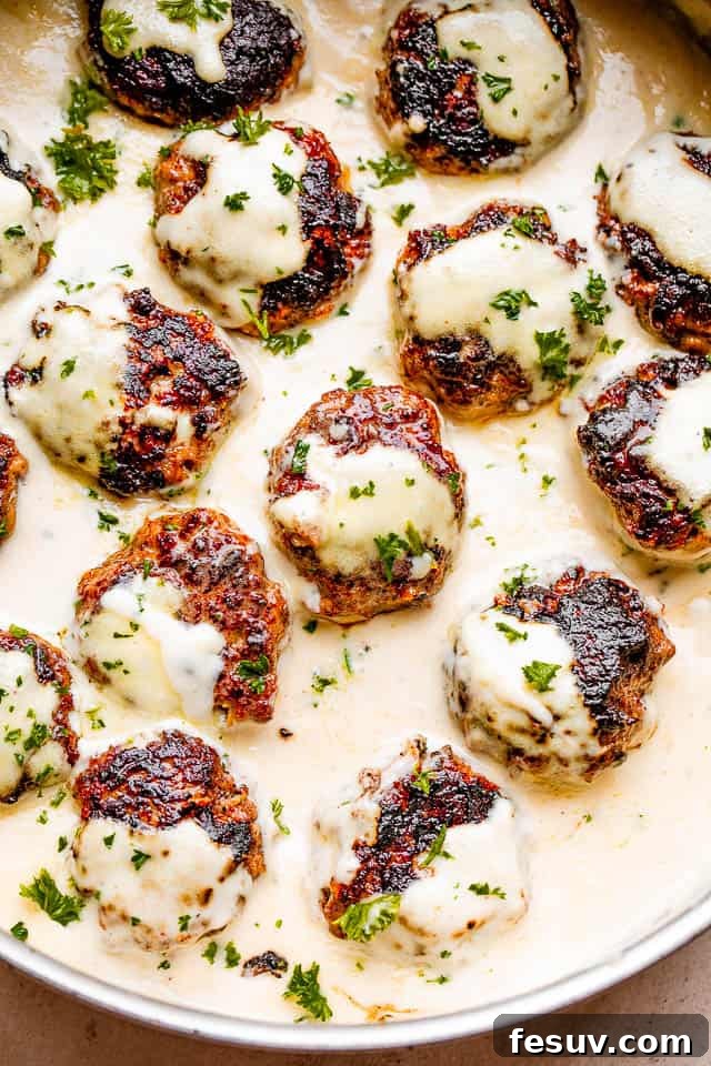 These homemade Swedish meatballs are bite size balls of beef and pork smothered in a rich, creamy gravy. A comforting and belly warming meal! Close-up of Swedish meatballs simmering in creamy sauce, garnished with fresh parsley