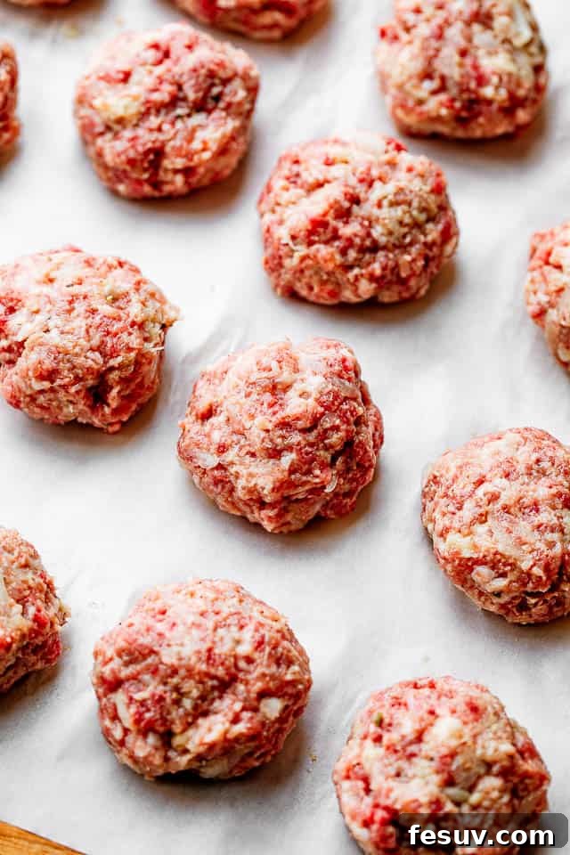 These homemade Swedish meatballs are bite size balls of beef and pork smothered in a rich, creamy gravy. A comforting and belly warming meal! Perfectly rolled raw Swedish meatballs arranged on white parchment paper, ready for cooking