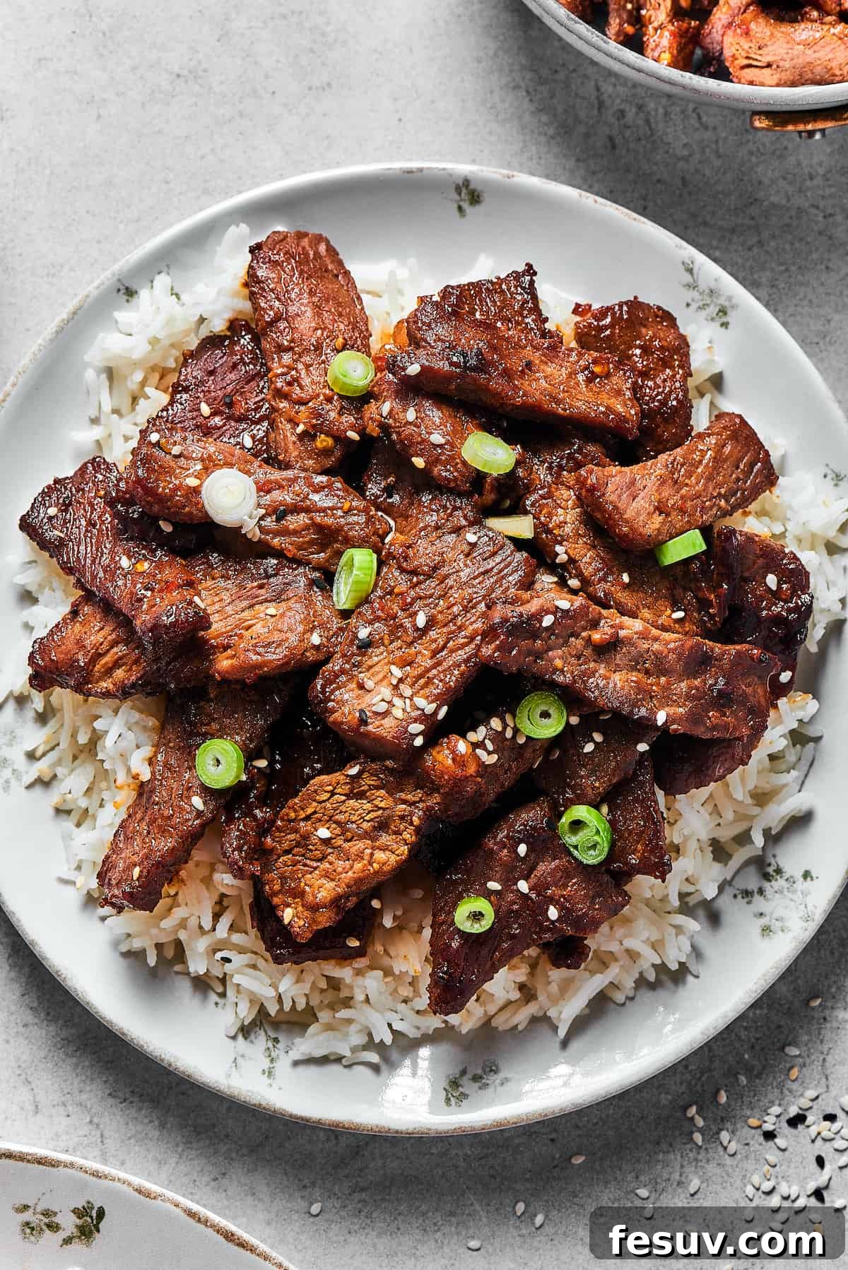 Beef bulgogi served onto a white plate, over a bed of rice.