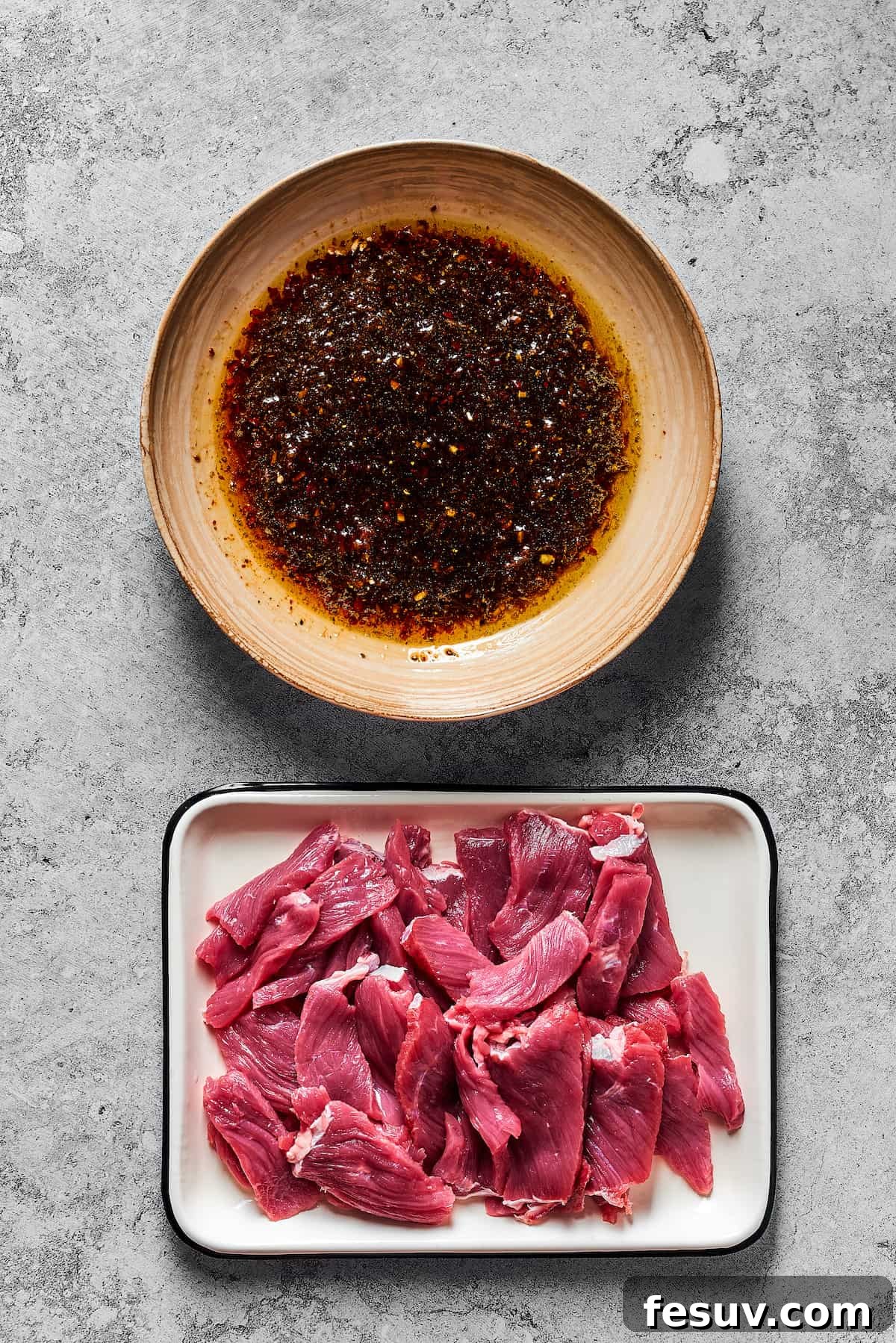 A bowl of marinade next to an enamel tray of sliced steak.