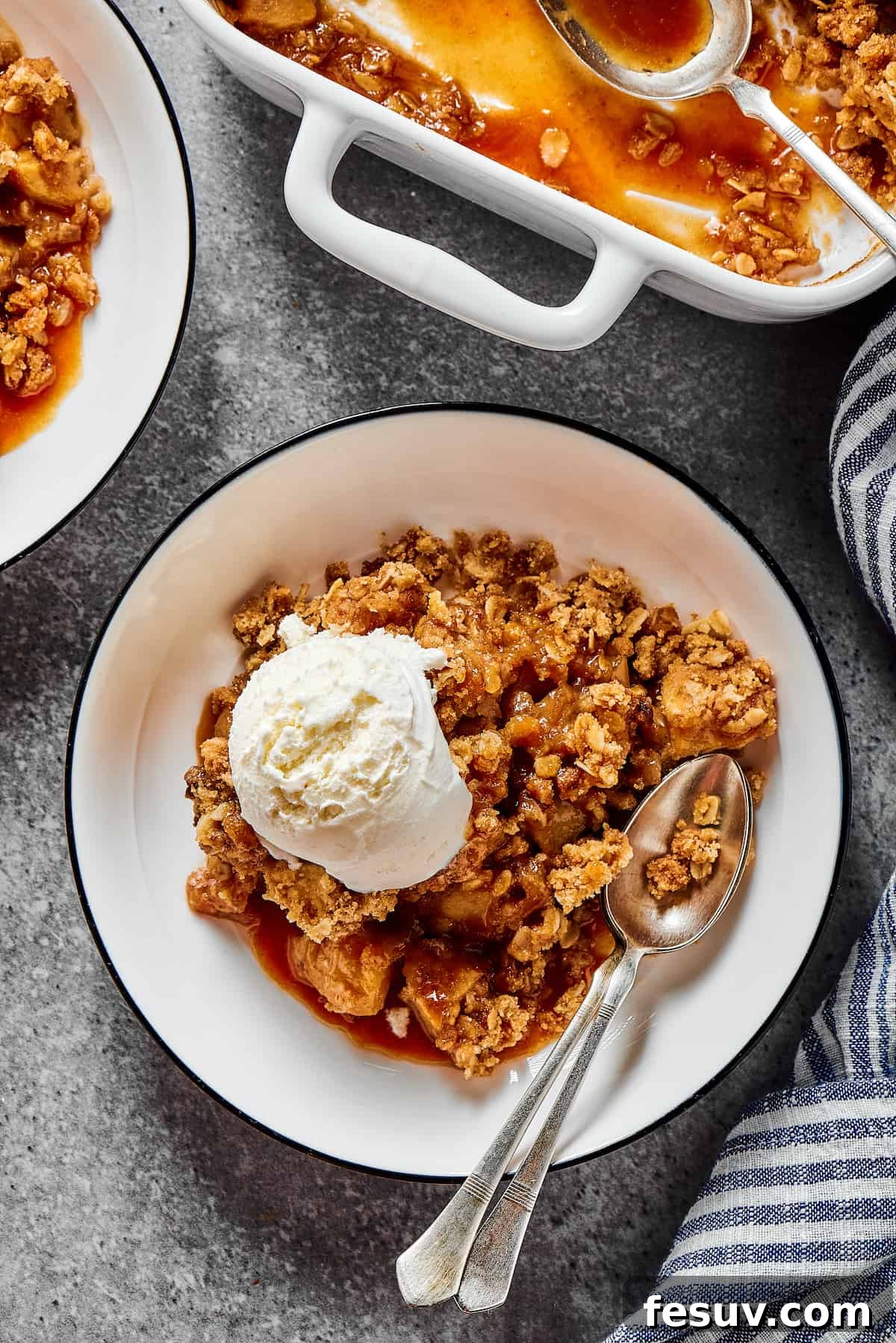 Scoops of vanilla ice cream melting over a warm, golden-brown apple crisp with a crunchy oat topping, served in an elegant dessert bowl.