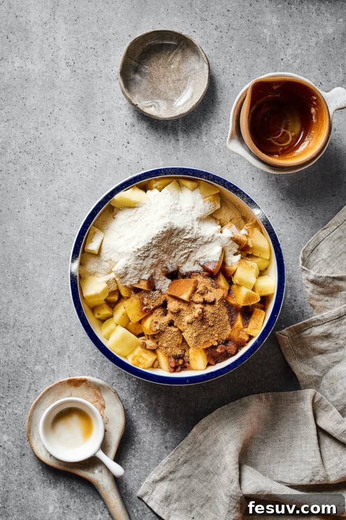 A large bowl containing chopped apples coated in a mixture of flour, butter, and warm spices, ready for baking.