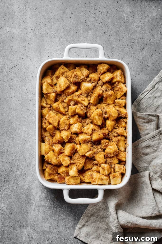A baking dish filled with a generous layer of spiced, floured apples, ready for the crisp topping to be added.