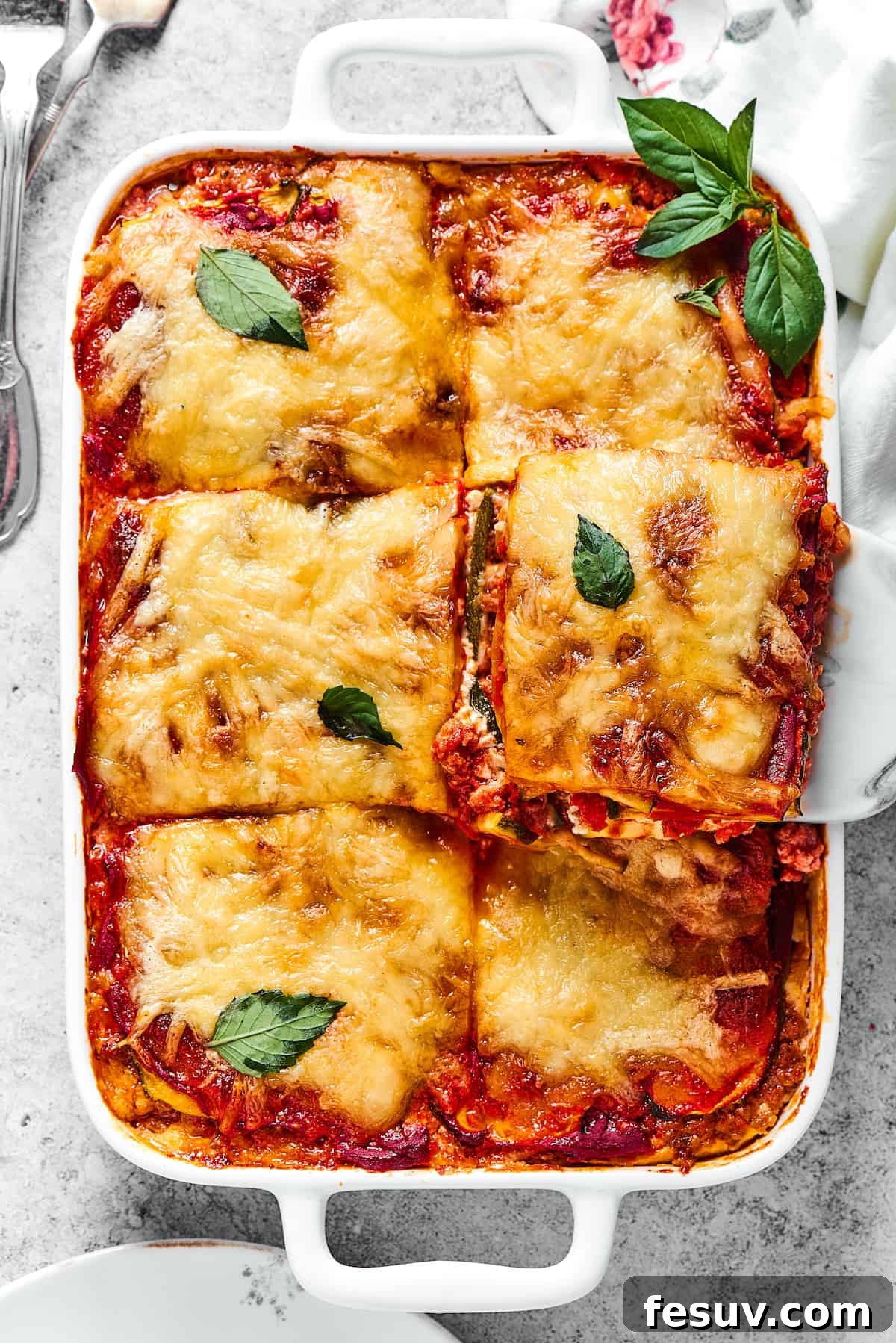 A comforting Zucchini Lasagna with rich meat sauce being served from a white rectangular baking dish, showcasing golden-brown cheese and tender zucchini layers.