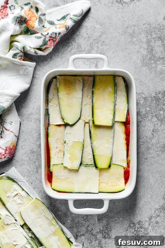 A neat layer of floured zucchini slices covering the base of tomato sauce in a baking dish.