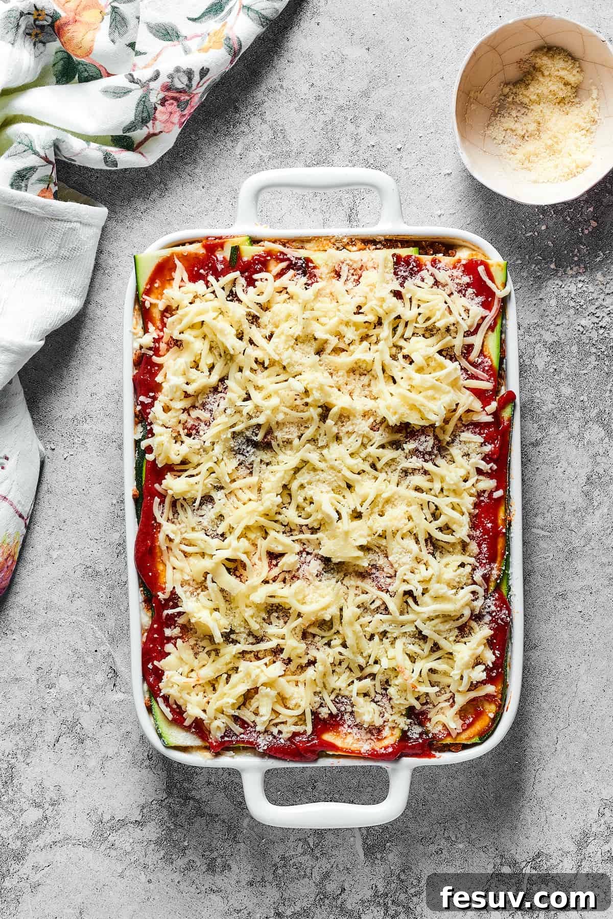 An unbaked zucchini lasagna, generously topped with shredded mozzarella, ready to be placed in the oven.