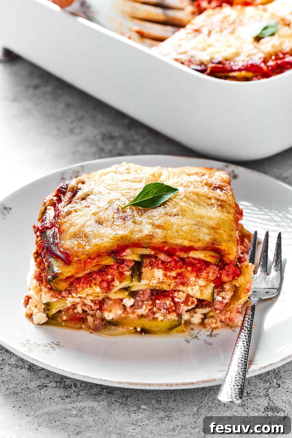 A perfectly portioned square of cheesy Zucchini Lasagna on a white plate, ready to be enjoyed.