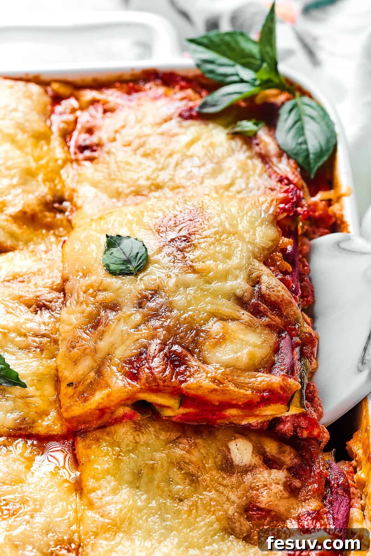 A glorious Zucchini Lasagna with meat sauce being carefully lifted from a white rectangular baking dish, showcasing its perfect layers.