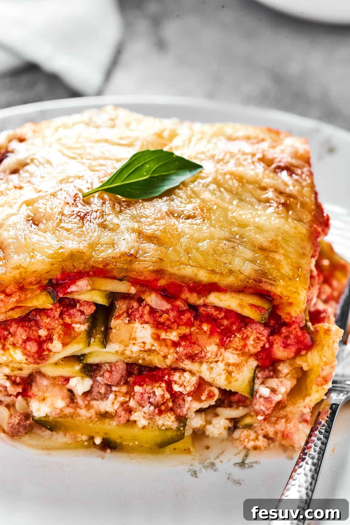 A tempting serving of Zucchini Lasagna on a white dinner plate, with a fork poised for a delicious bite.