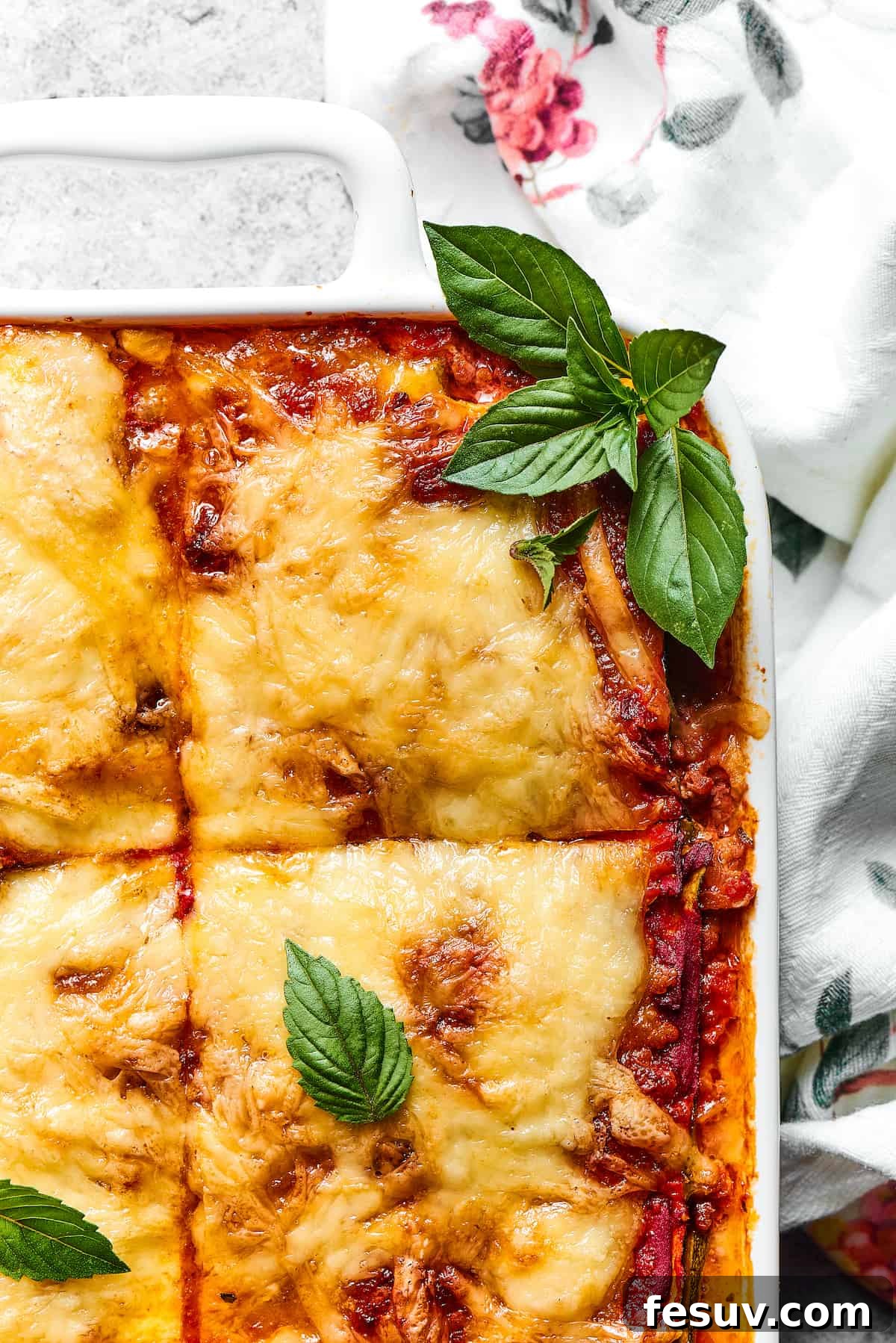 A close-up view of a slice of Zucchini Lasagna, garnished with fresh basil, showing the delicious layers of meat sauce, cheese, and zucchini.