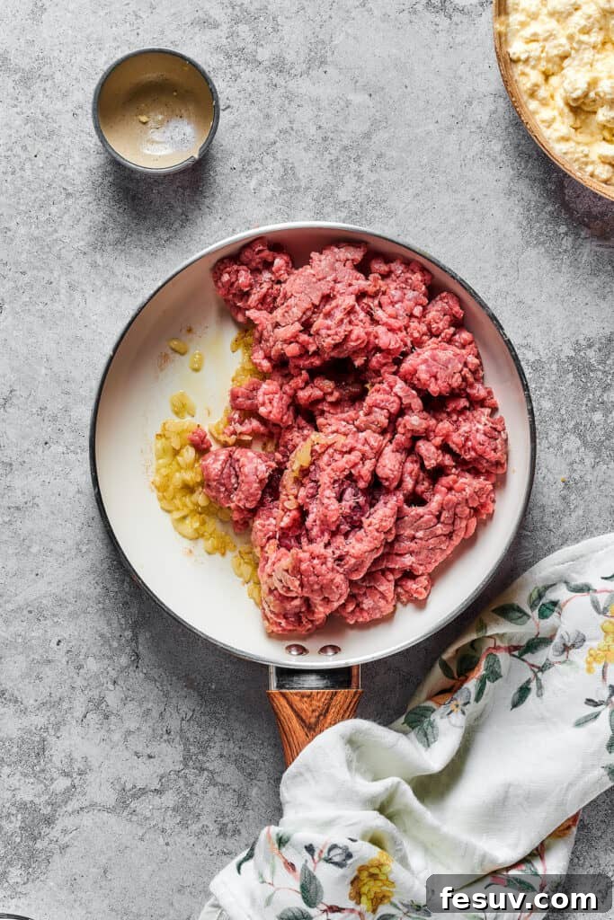 Garlic, onions, and ground beef sizzling together in a skillet, forming the base of the rich meat sauce.