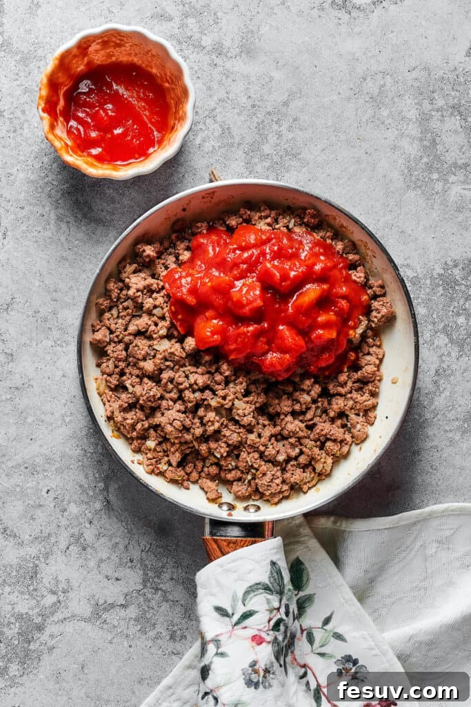 Hearty meat sauce simmering in a skillet, featuring crushed tomatoes and savory seasonings, ready for layering.