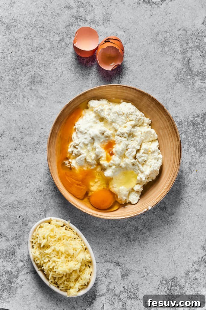 A bowl filled with a creamy cheese mixture of cottage cheese, Parmesan, and eggs, alongside a smaller bowl of shredded mozzarella.