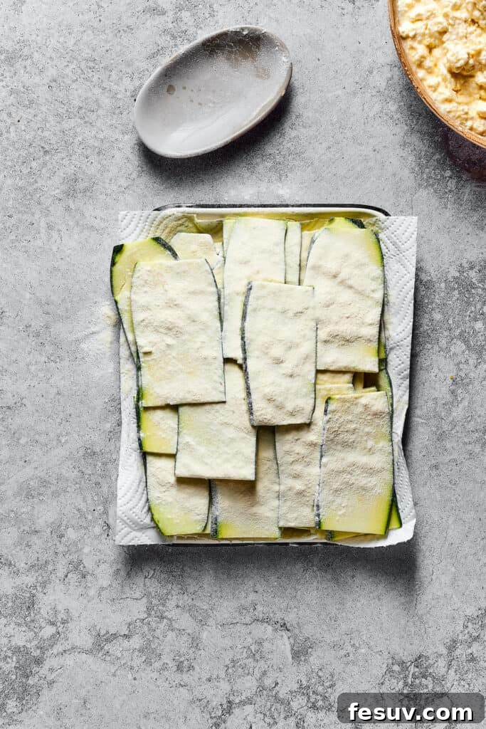Thin strips of lightly floured zucchini resting on a paper-towel-lined tray, prepped for layering in the lasagna.