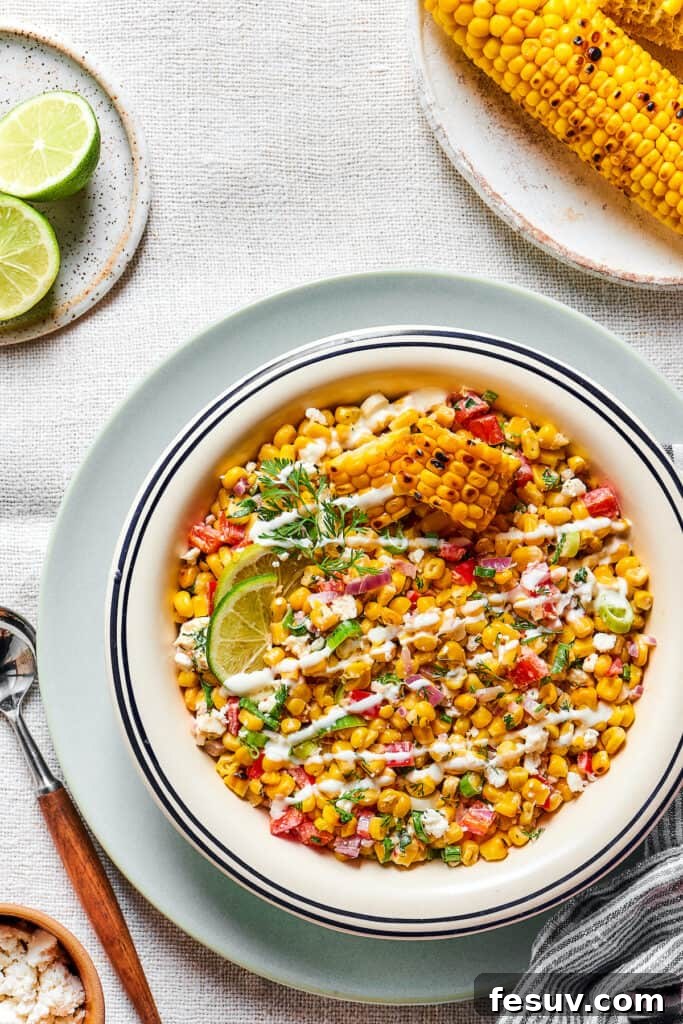 Zesty Mexican Street Corn Salad 5 Mexican street corn salad in a serving bowl, garnished with dressing and lime wedges.