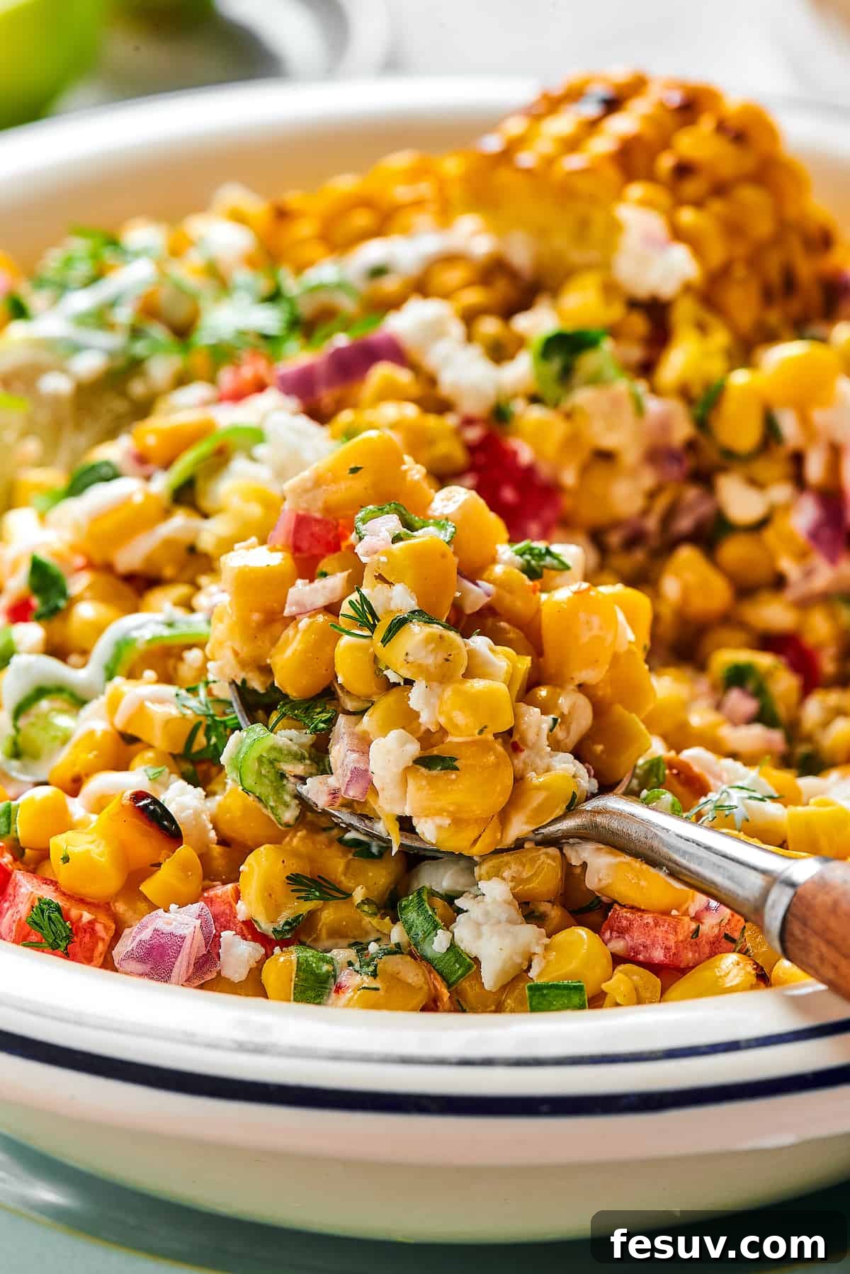 Mexican Street Corn Salad is a mouthwatering dish that’ll have everyone begging for the recipe! Fresh corn kernels in a killer creamy sauce. A spoonful of grilled corn salad being lifted toward the camera from a serving dish, highlighting its fresh ingredients.