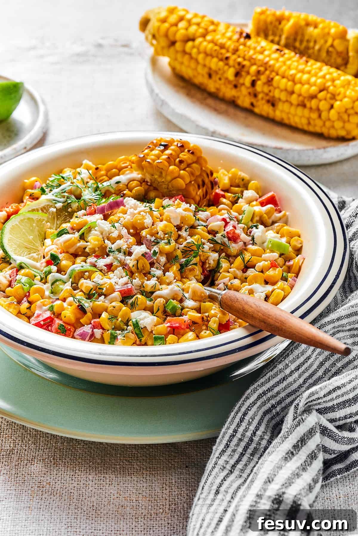 Mexican Street Corn Salad is a mouthwatering dish that’ll have everyone begging for the recipe! Fresh corn kernels in a killer creamy sauce. Elote salad in a bowl with a wooden-handled spoon, ready to be served.