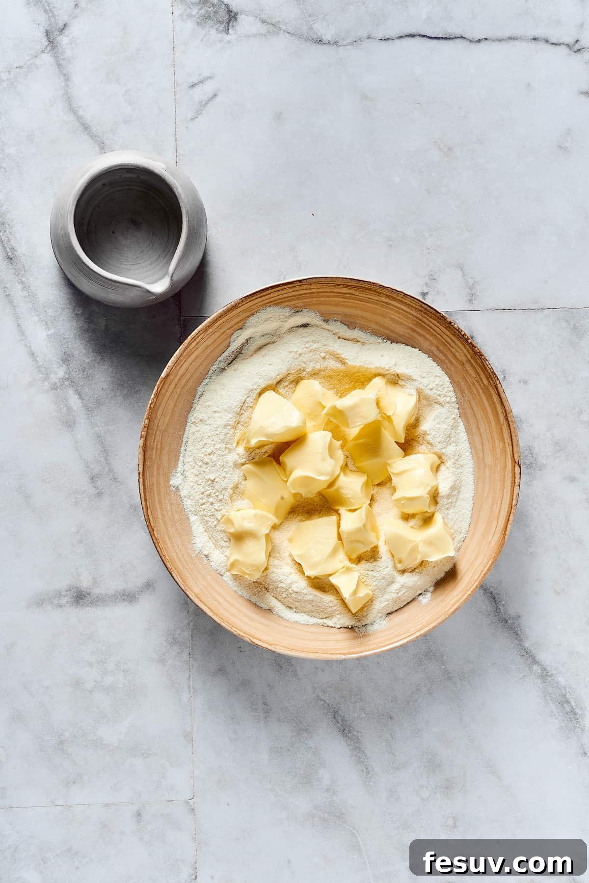 Diced cold butter being added to the dry baking ingredients in a mixing bowl.
