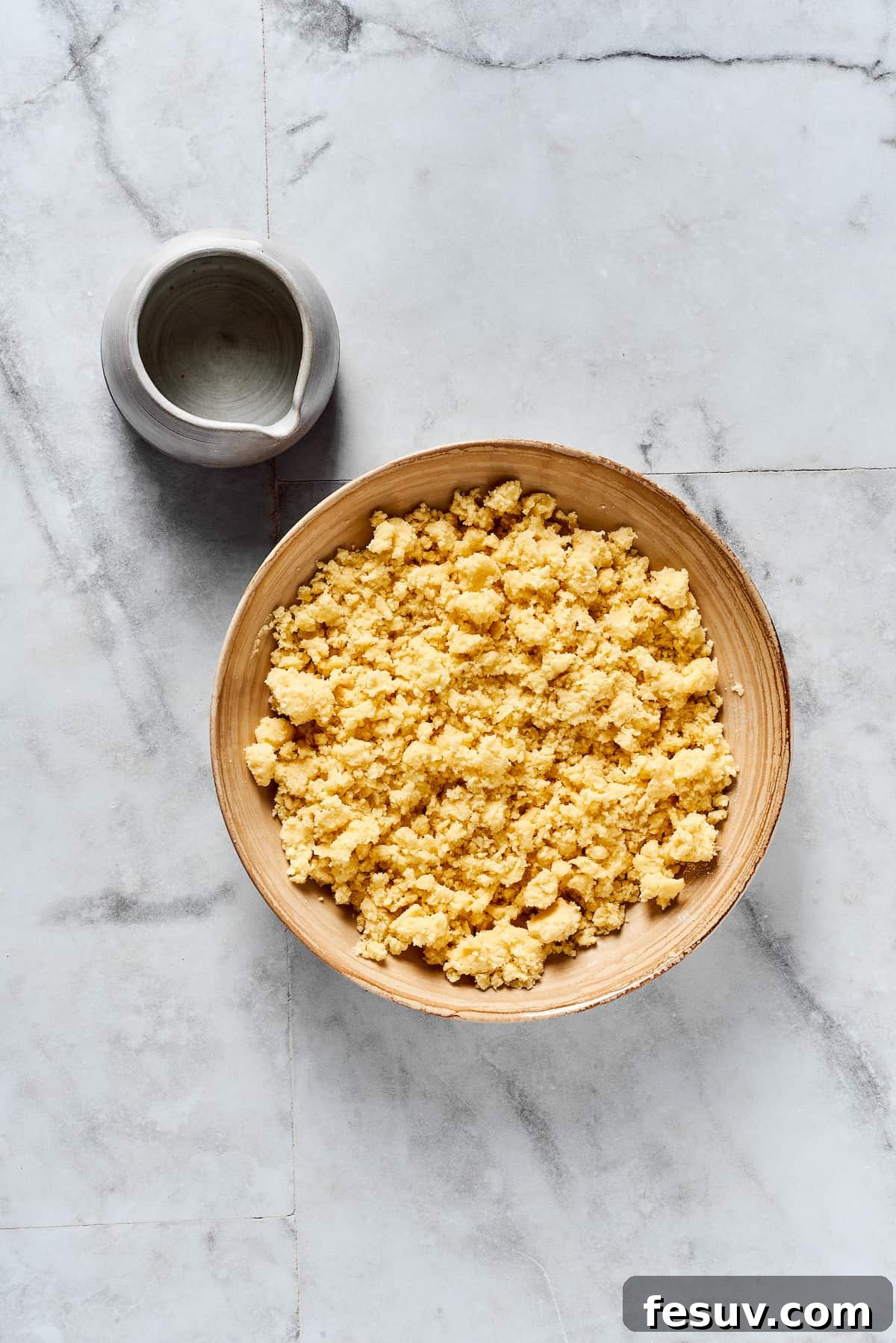 A close-up of crumbly pie dough with visible butter pieces, before being pressed together.