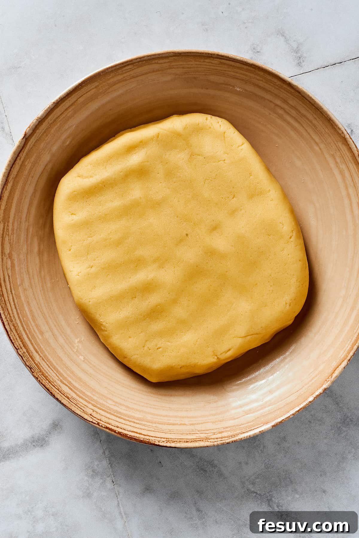 A flattened disc of pie dough wrapped in plastic, ready for chilling in a mixing bowl.