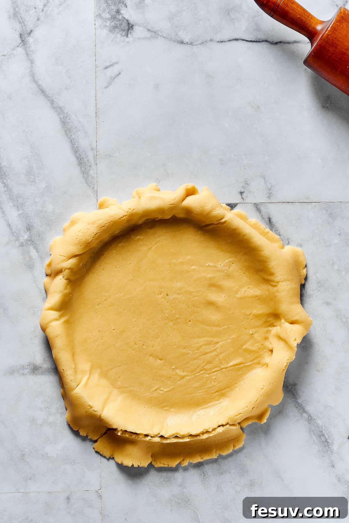 A rolled-out pie crust draped over a pie plate, with the edges overhanging.