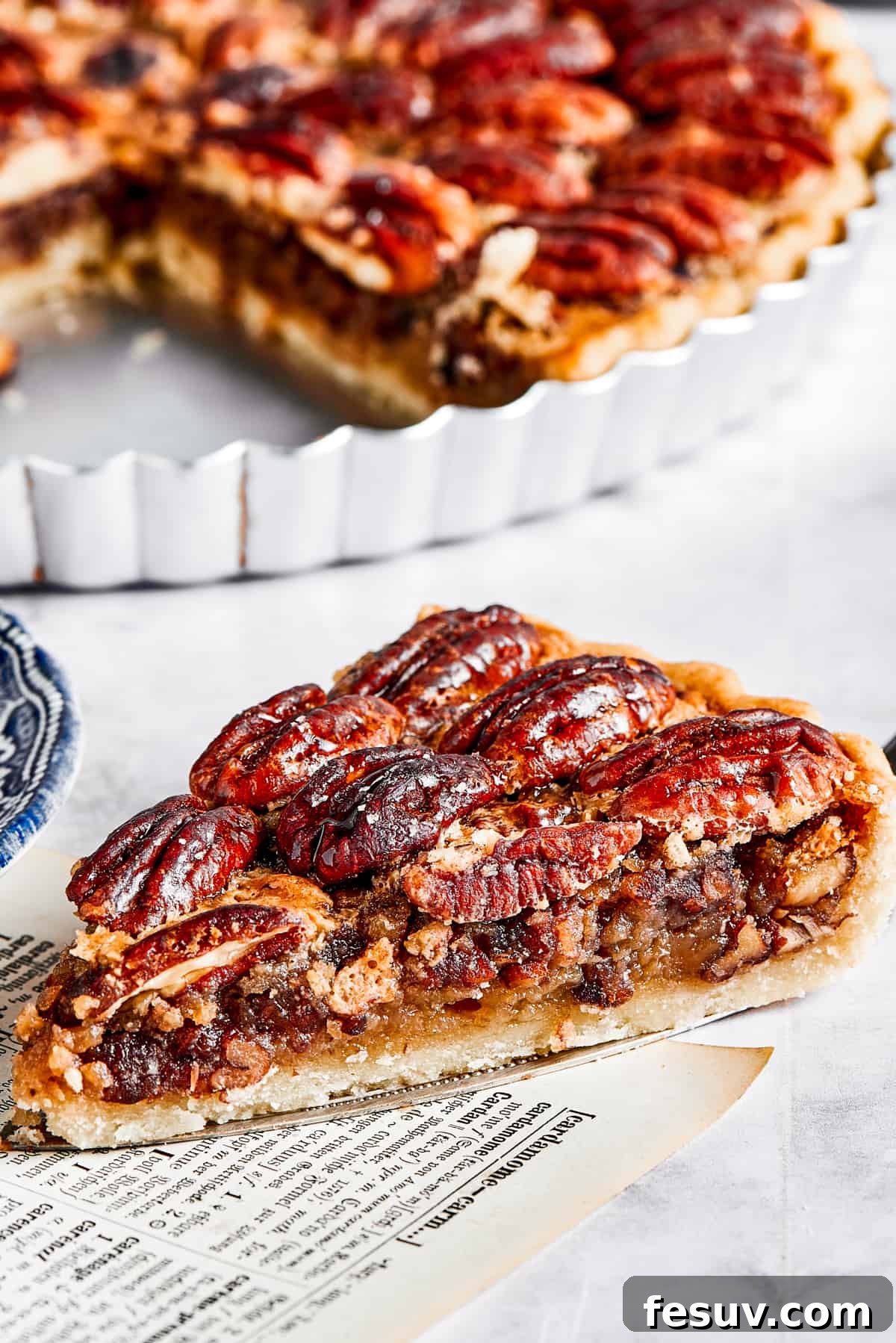 The Best Pecan Pie Recipe is here, easy to make and perfect for your holiday table! You'll love the homemade crust and sweet, nutty filling. A slice of pie on a pie server, next to the pie dish.