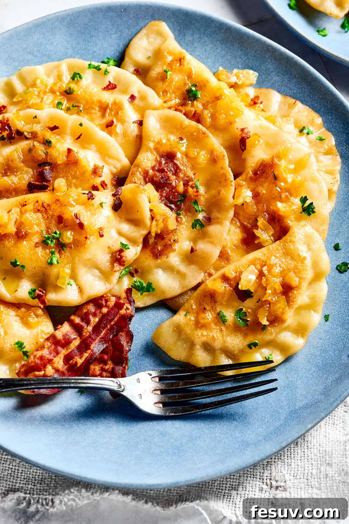 Topped with caramelized onion and crispy bacon, this easy Homemade Pierogi Recipe features a traditional cheese and potato filling. Yum! Bacon and onion topped pierogi ruskie, a classic homemade dish.
