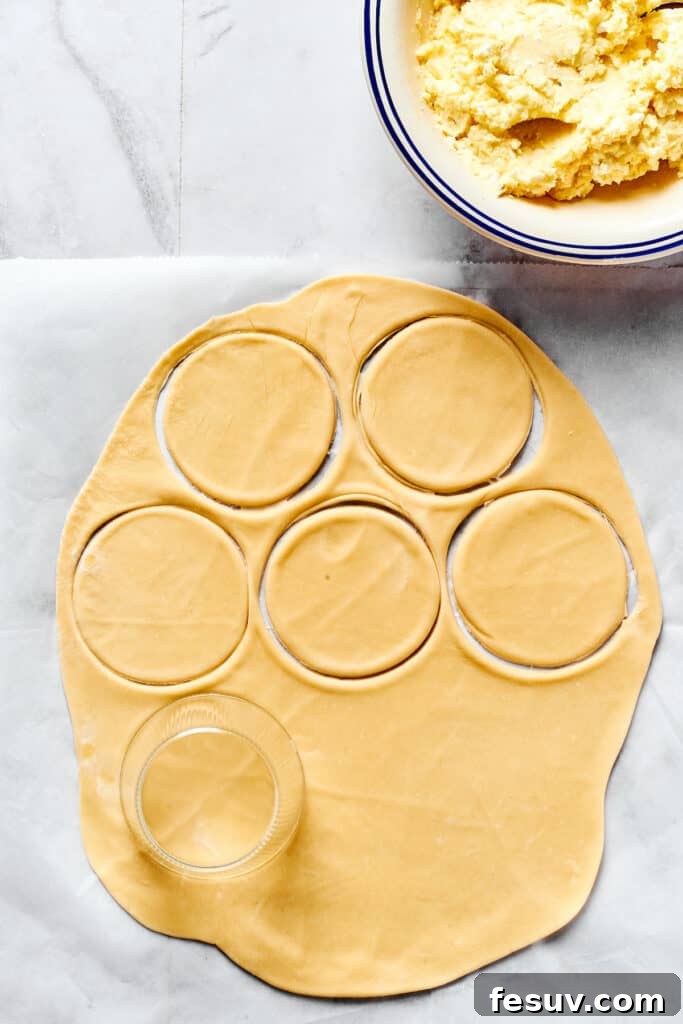 Handcrafted Pierogi Delights 6 A sheet of thinly rolled pierogi dough on a work surface, with rounds cut out and a bowl of cheesy potato filling nearby, ready for assembly.