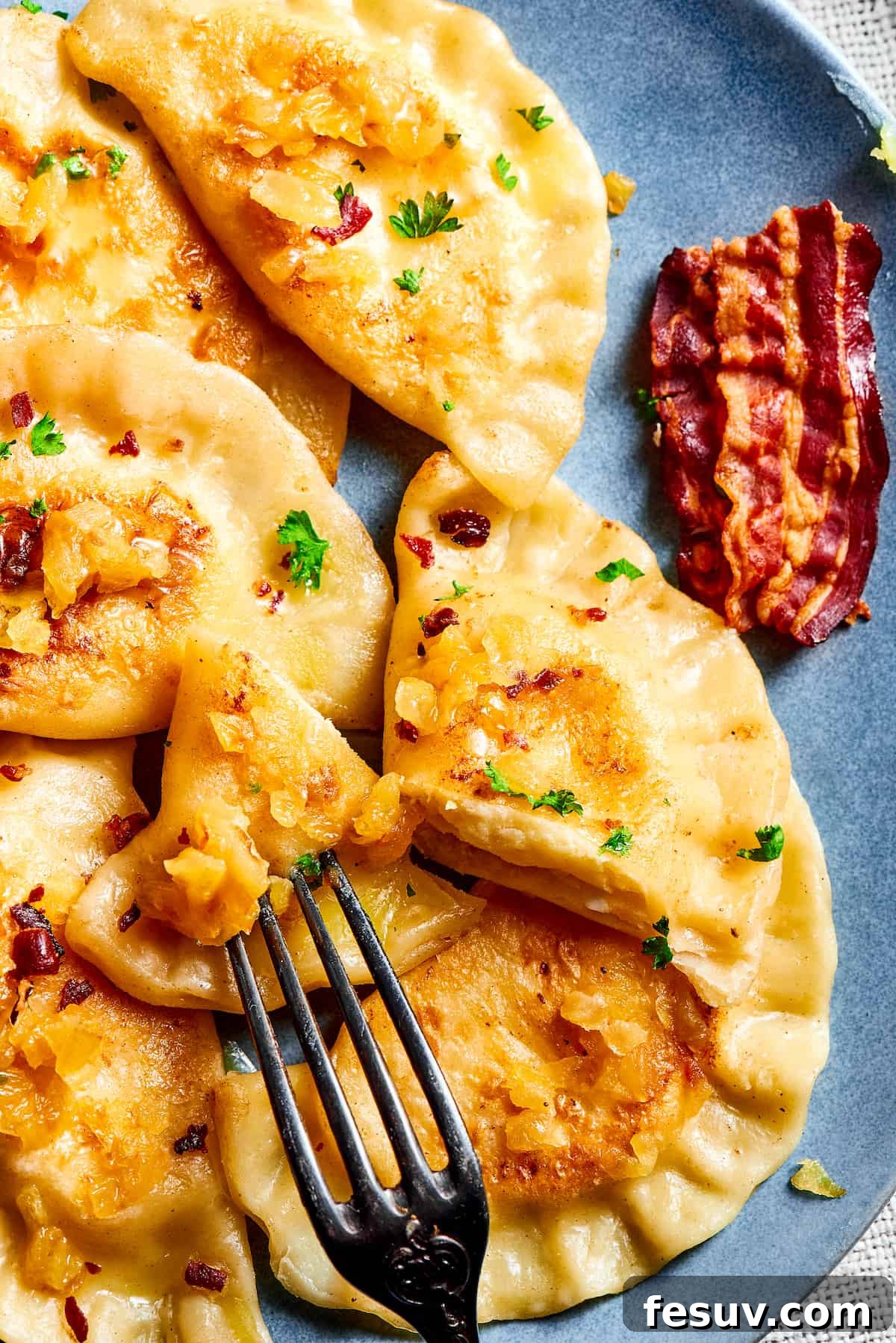 Topped with caramelized onion and crispy bacon, this easy Homemade Pierogi Recipe features a traditional cheese and potato filling. Yum! A fork cutting into a homemade potato and cheese dumpling, revealing its soft interior.