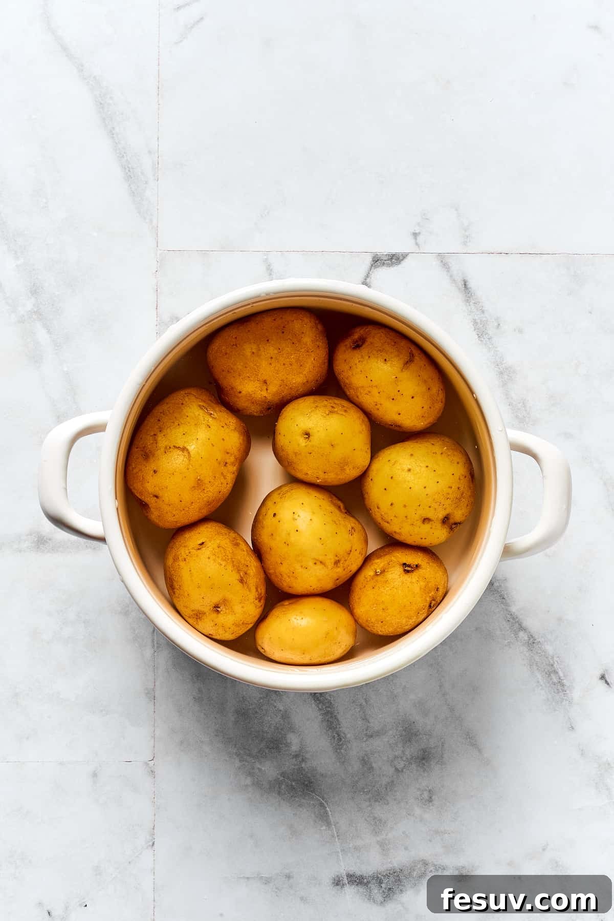 Topped with caramelized onion and crispy bacon, this easy Homemade Pierogi Recipe features a traditional cheese and potato filling. Yum! Potatoes cooking in a pot on the stovetop.