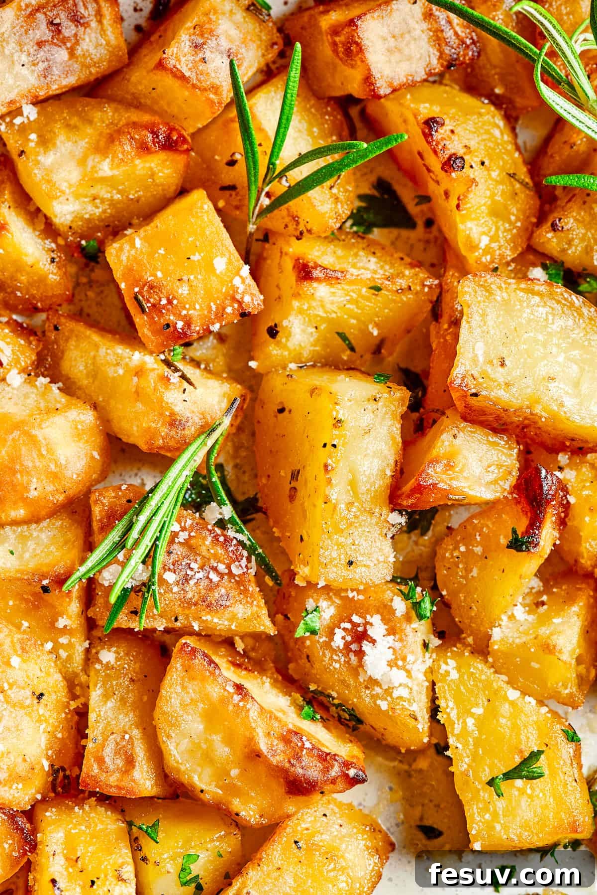 ed Potatoes are crisp, buttery, and easy to make. With a simple seasoning of salt, pepper, and rosemary, they're irresistible! close up shot of oven roasted potatoes garnished with rosemary leaves and grated cheese.