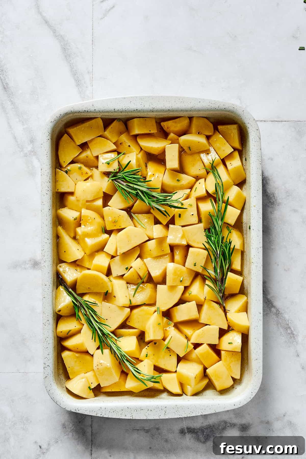 Foolproof Roasted Potatoes 4 Seasoned raw potatoes and rosemary sprigs in a baking dish.