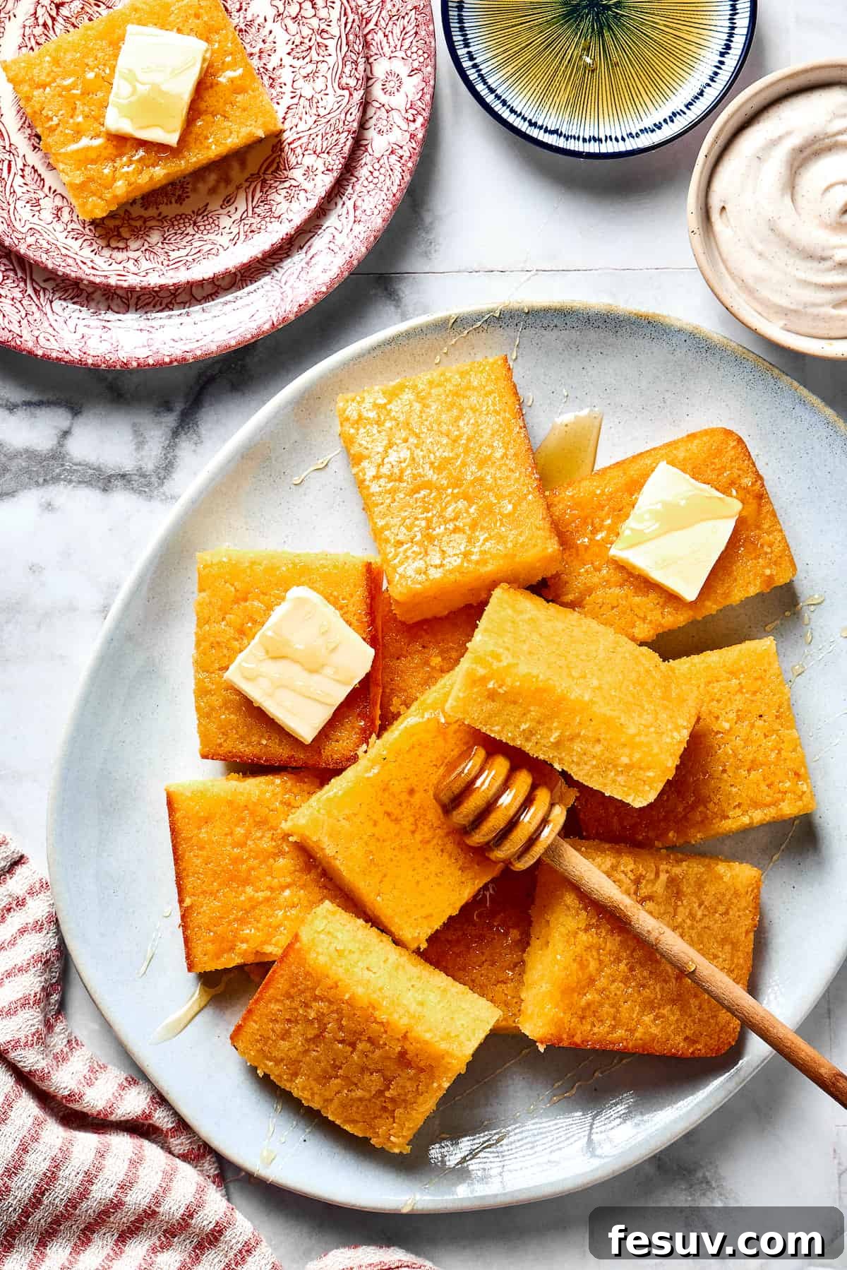 Perfectly baked squares of golden cornbread arranged on a rustic plate, accompanied by pats of melting butter and a honey dipper, ready to be enjoyed.
