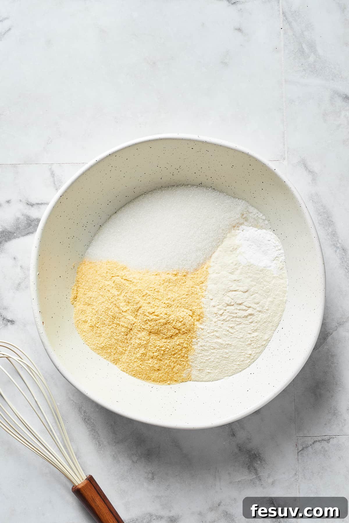 A bowl filled with the combined dry ingredients for cornbread, including flour, cornmeal, sugar, baking powder, and salt, ready for the wet ingredients.