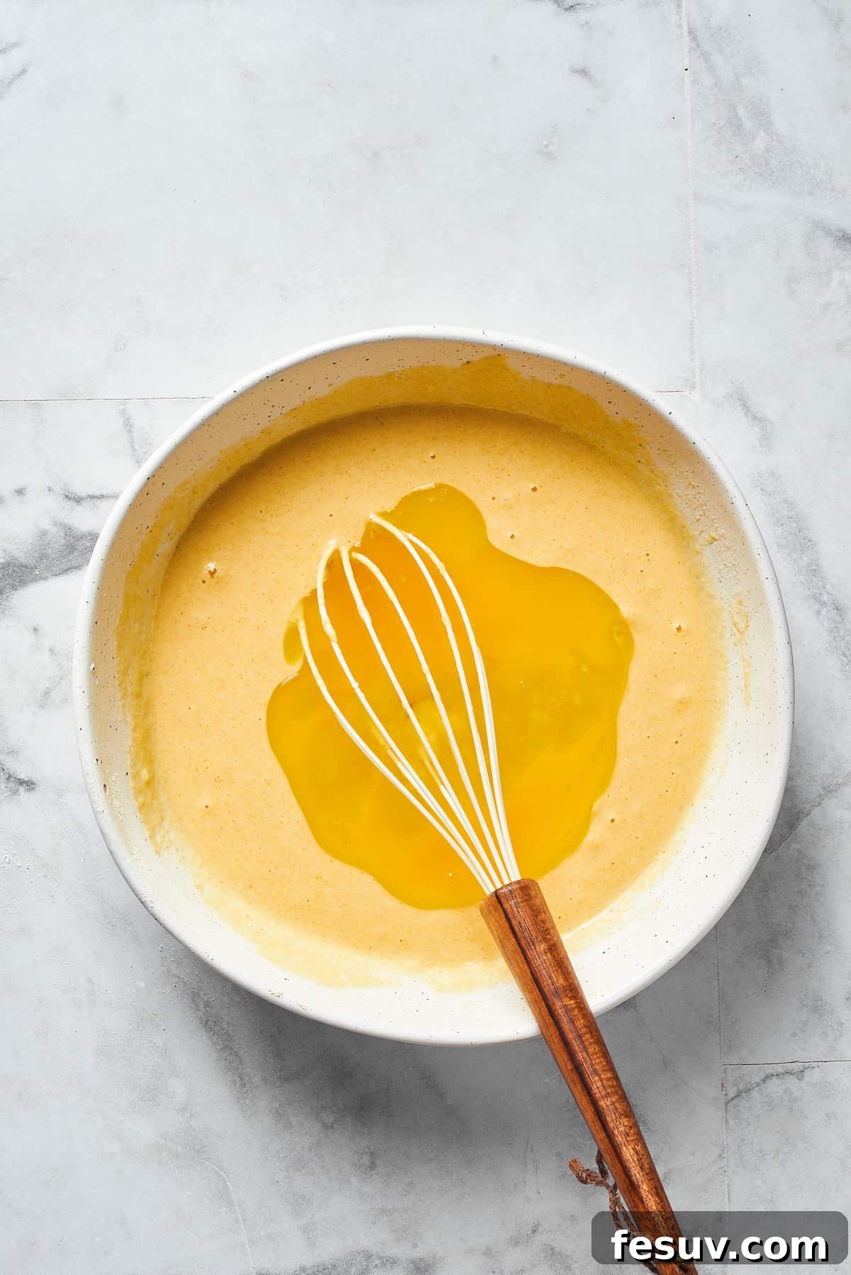 A whisk creating a well in the center of the dry cornbread ingredients, preparing for the addition of the liquid mixture.